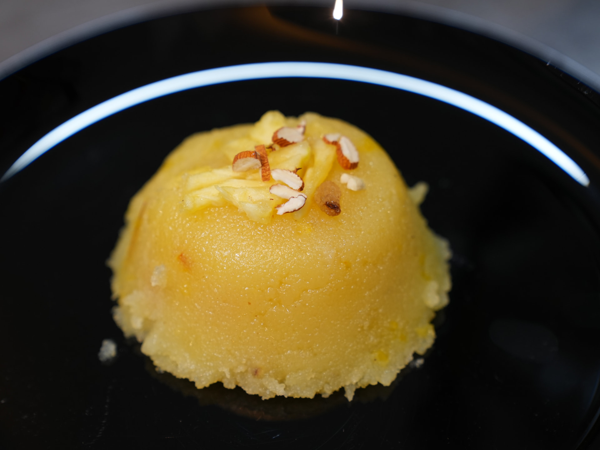 A plated kesari mound on a black plate topped with almond slivers and raisin