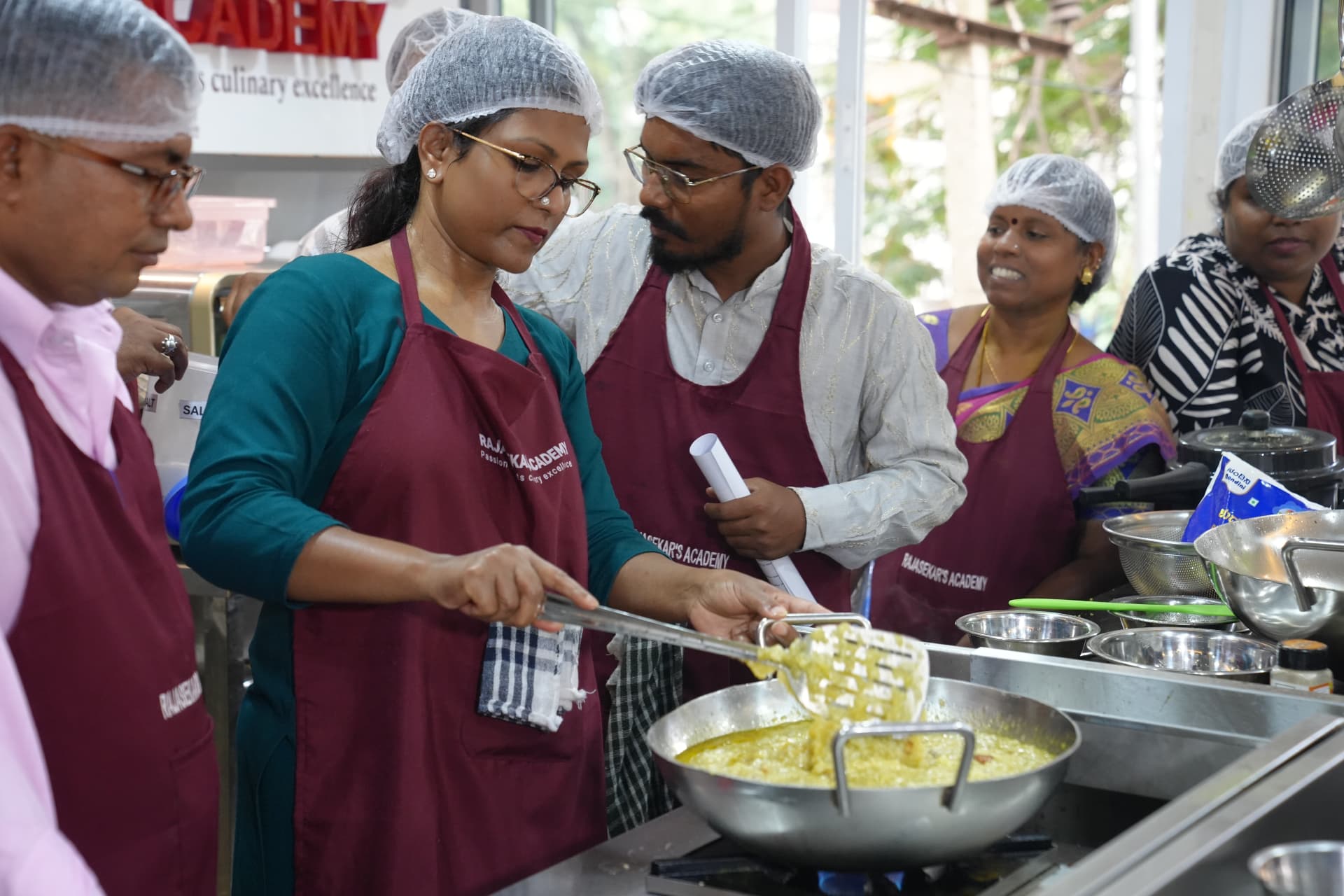 Students in academy aprons cooking together under Chef Rajasekar's guidance
